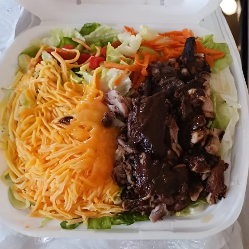 A Tropical Jerk salad with shredded cheese, lettuce, carrots, tomatoes, and dark meat chicken.