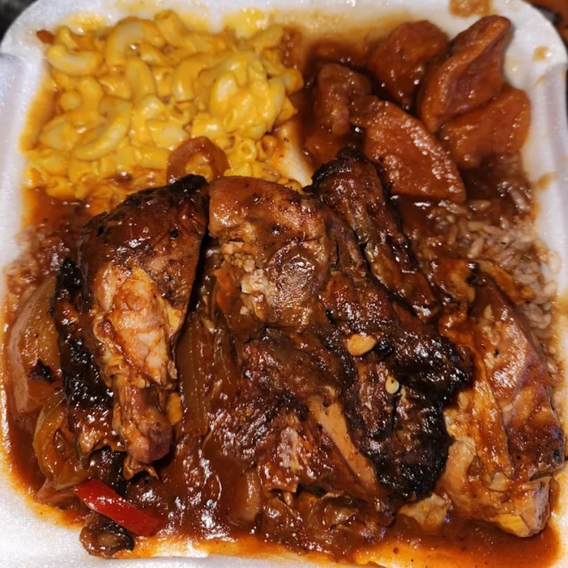 A takeout container filled with Jamaican jerk chicken, mac and cheese, rice, and plantains.